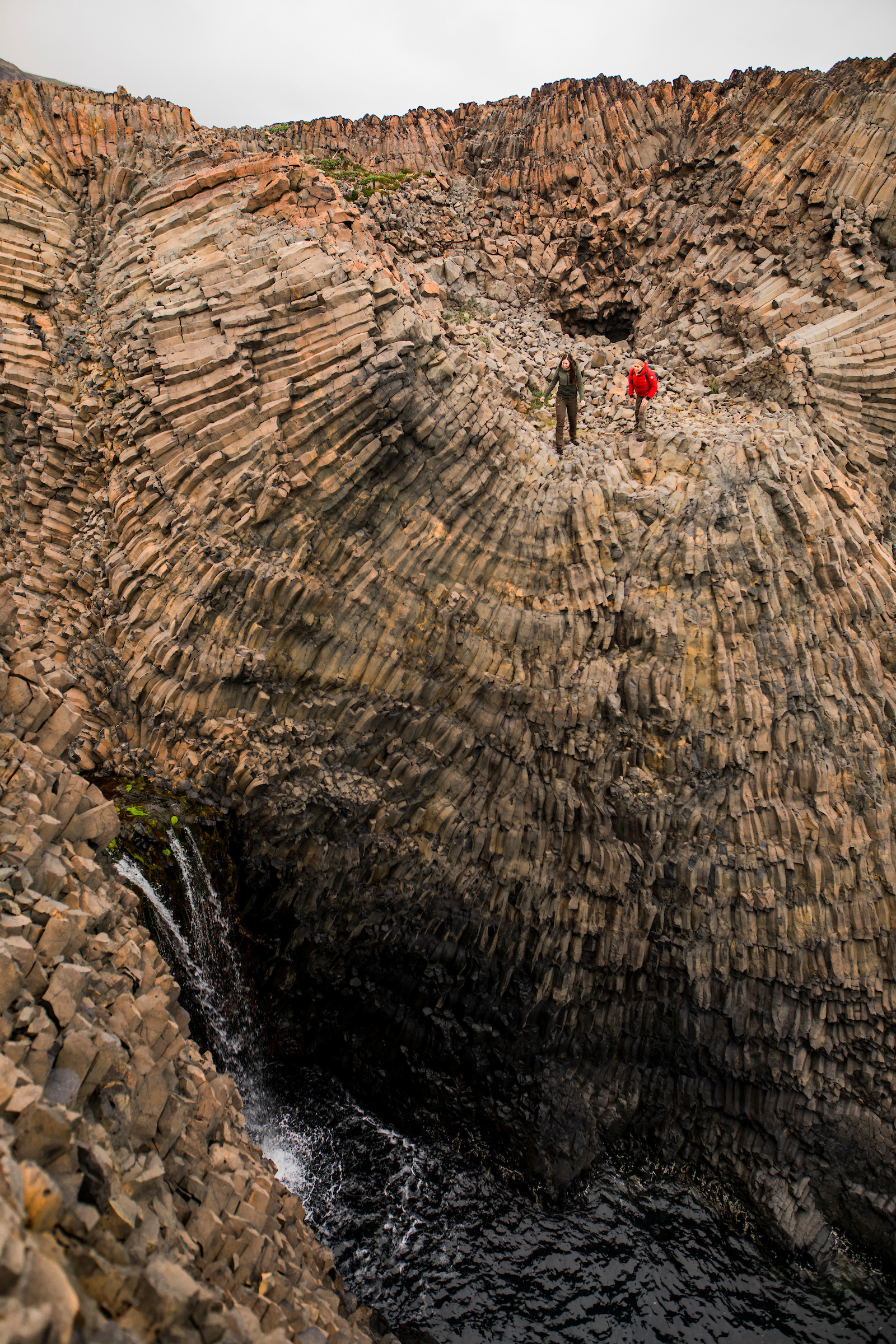 Two hikers exploring a waterfall between the Basalt columns, Disko Island